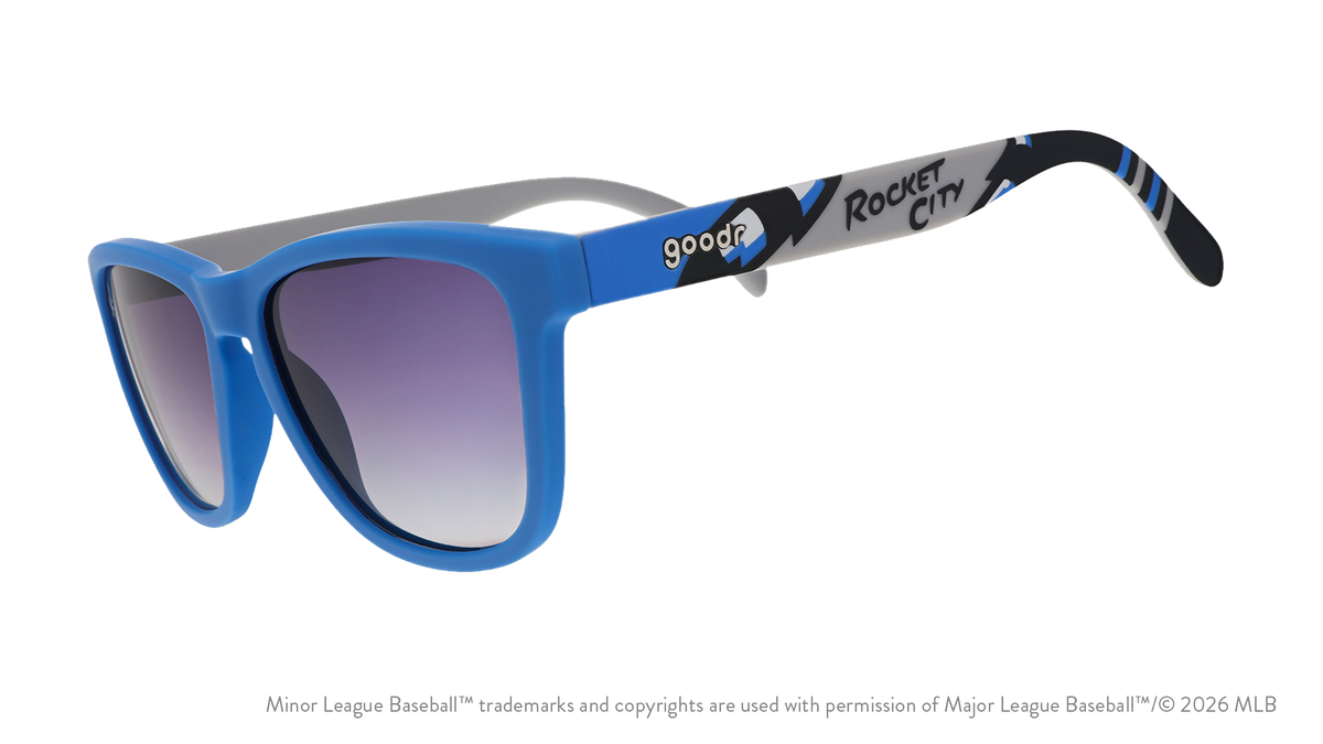 Three-quarter angle view of sunglasses tilted down. Blue frames w/ Rocket City on temples + black gradient lenses.