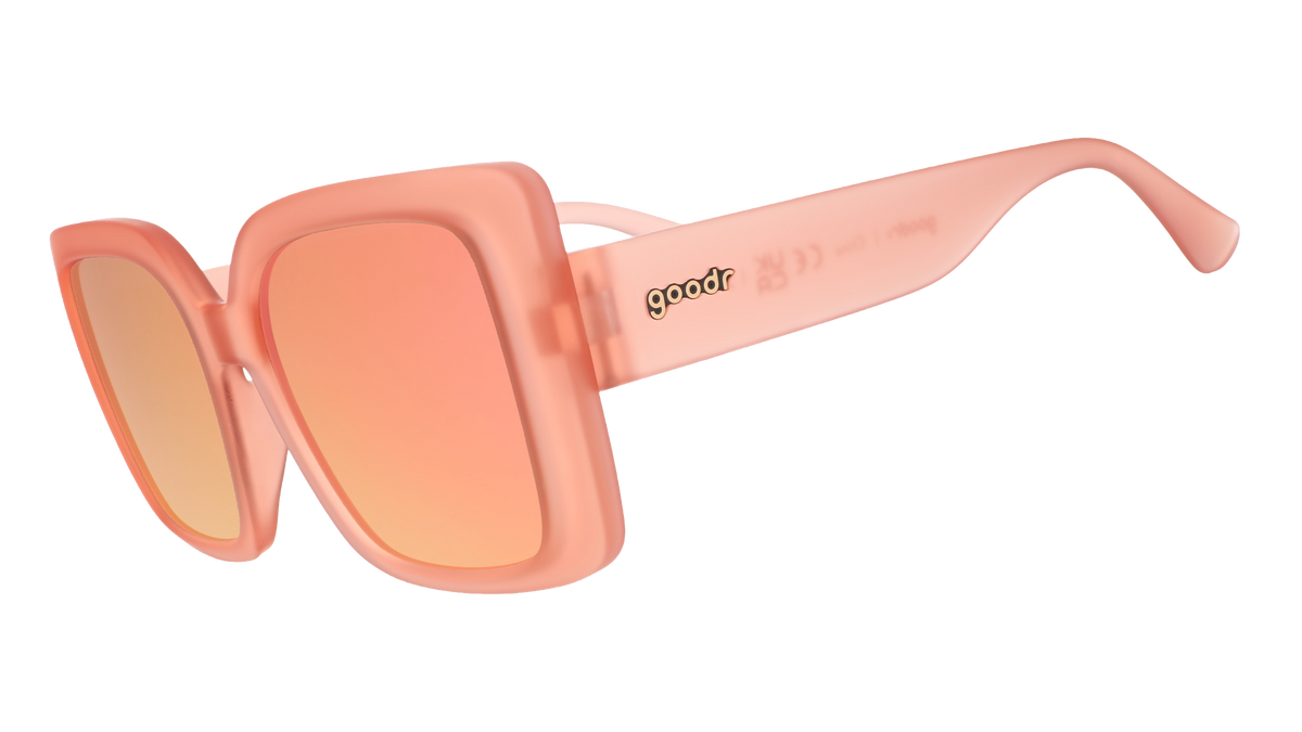 Three-quarter angle view of oversized square sunglasses in coral pink with champagne gold reflective lenses.