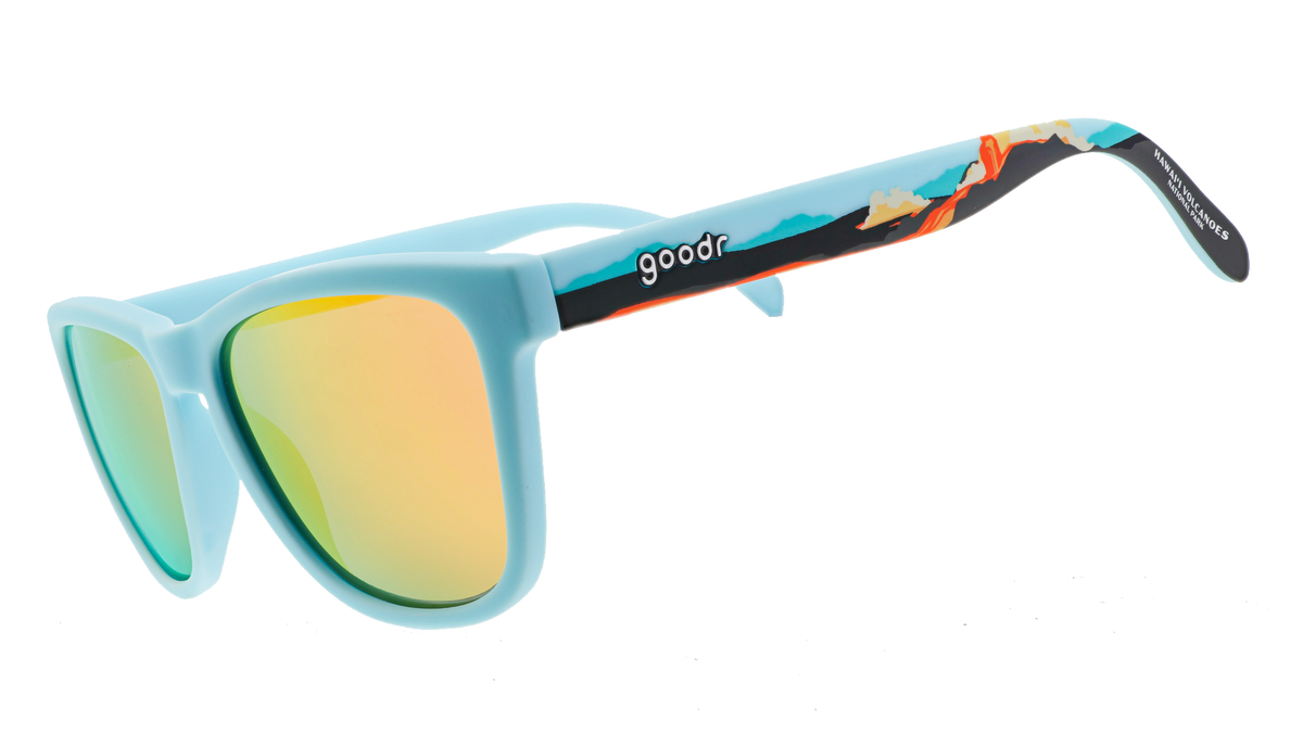 Pair of sunglasses with light blue frames and reflective yellow-orange lenses. The arms feature a vibrant tropical design with illustrations of waves and a sunset gradient.