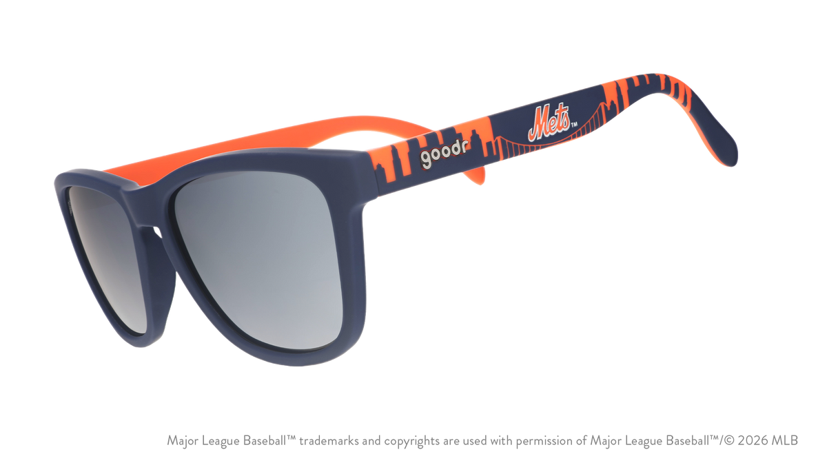 Three-quarter angle view of blue and orange Mets sunglasses featuring the script logo and a New York City skyline on the arm.