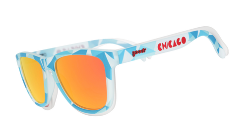 Three-quarter angle view of translucent blue, geometric-patterned sunglasses with burnt orange reflective lenses and Chicago logo.