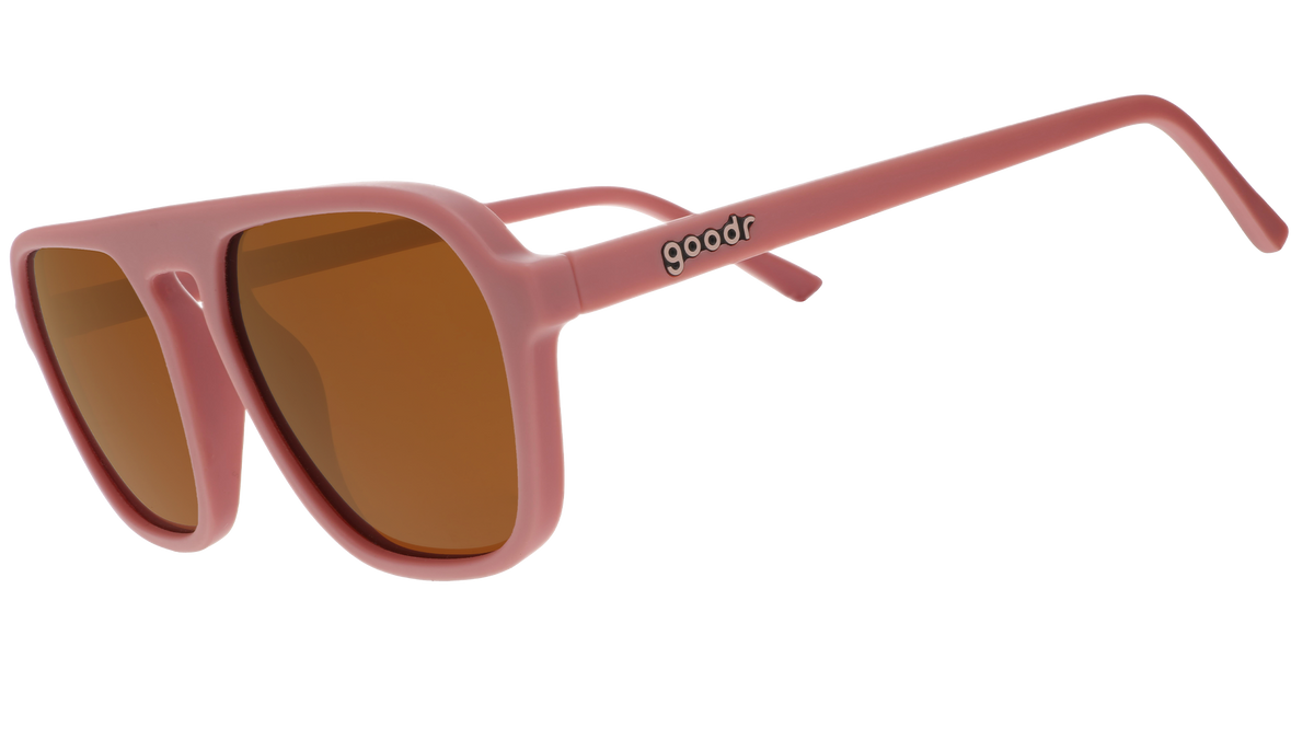 A pair of dusty rose pink goodr sunglasses with muted orange lenses on a white background.