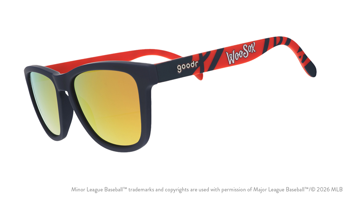 Three-quarter angle view of shades. Dark blue frames w/ a red pattern, WooSox on temples + amber reflective lenses.