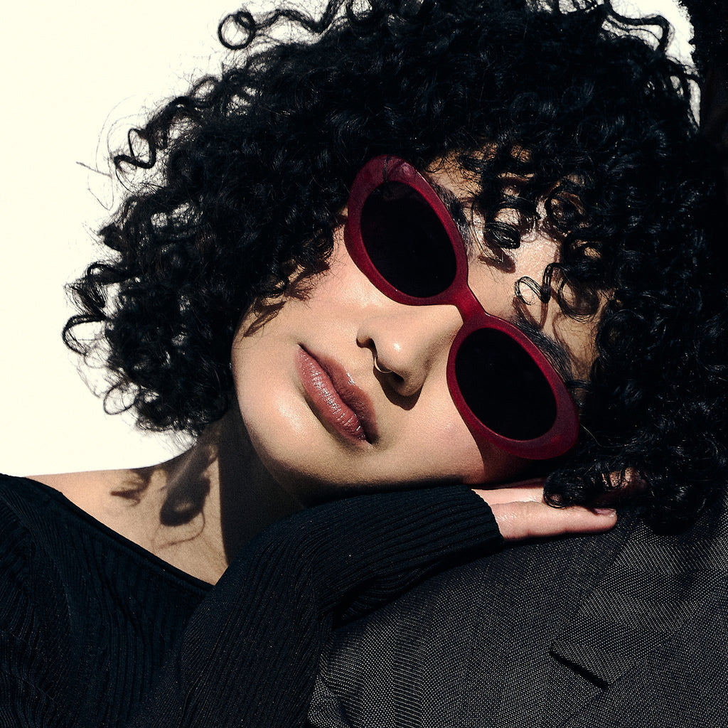 A woman poses while wearing hot pink oval sunglasses with dark red polarized lenses.