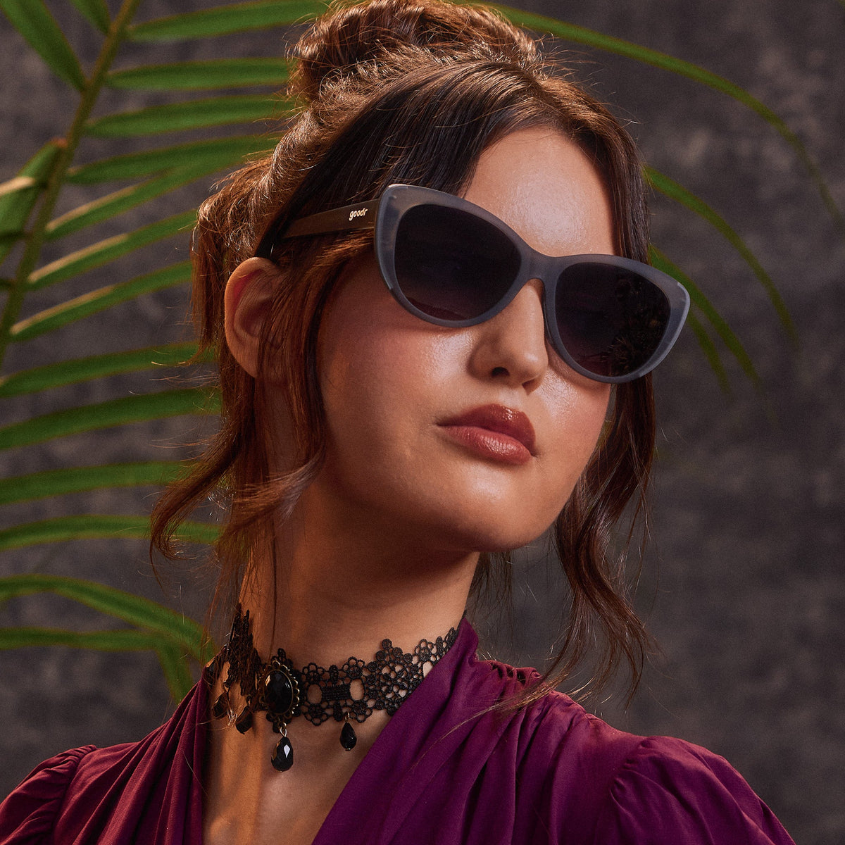 An elegantly dressed woman in translucent gray cat-eye sunglasses with black gradient lenses.