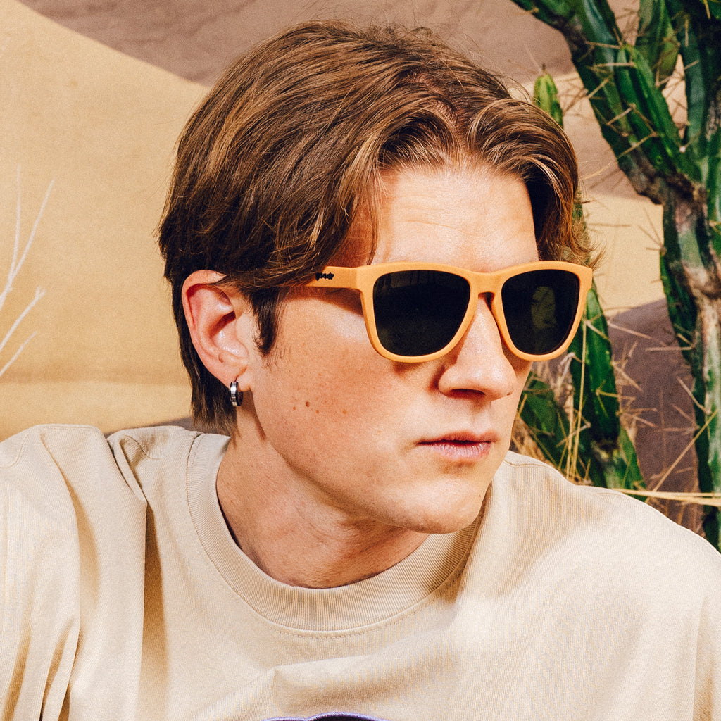 Side profile of a man wearing classic brown sunglasses with green non-reflective lenses in front of a desert backdrop.
