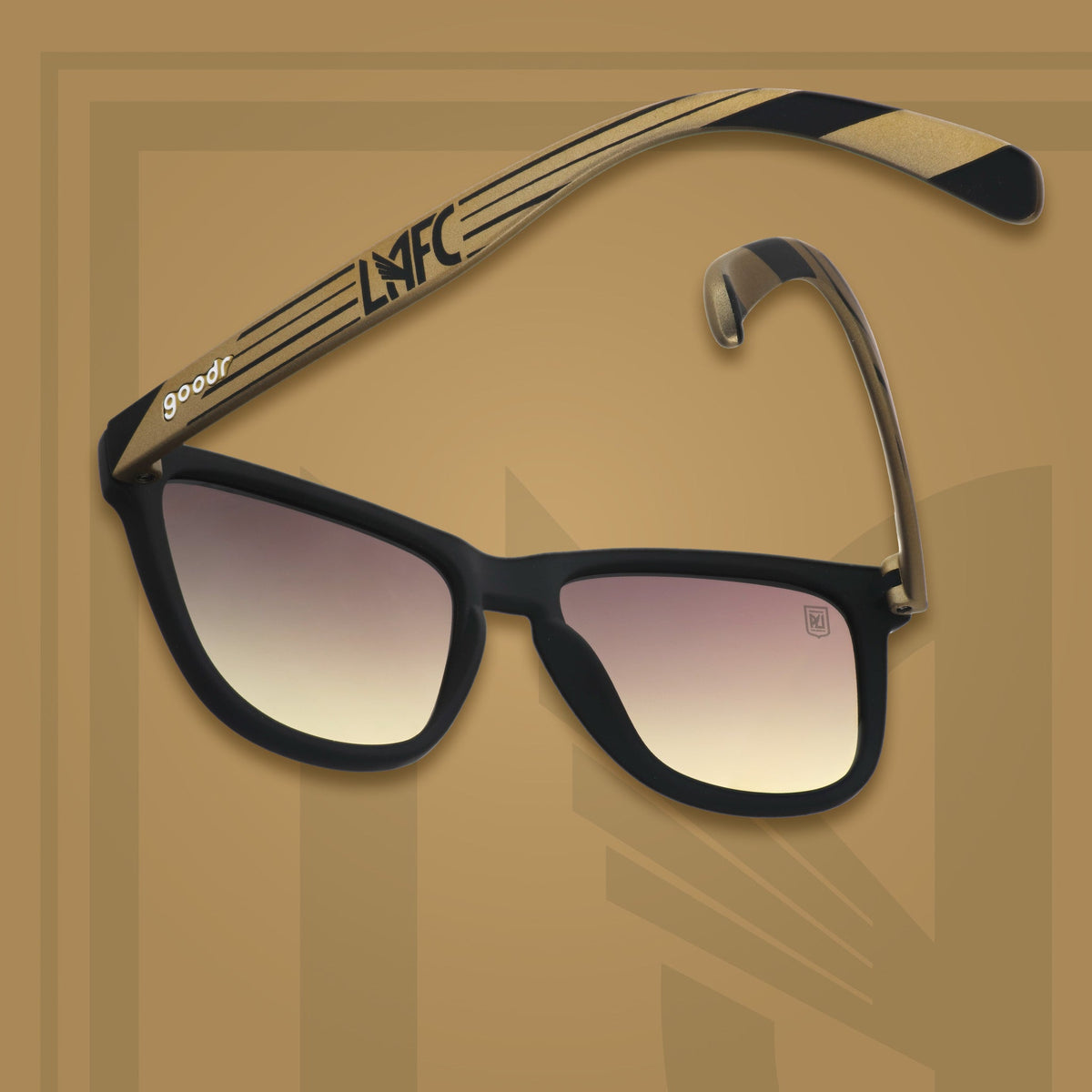 Three-quarter angle view of LAFC shades tilted down. Black and gold frames. Gray-yellow lenses. Gray-yellow background.