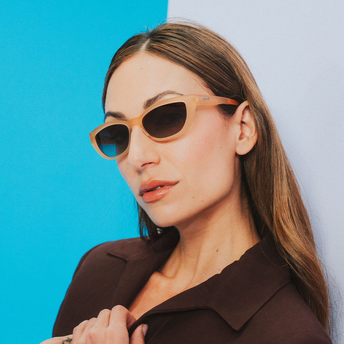A long-haired woman wearing a brown shirt and translucent brown cat-eye Cheetah Gs cocks her head confidently to one side.
