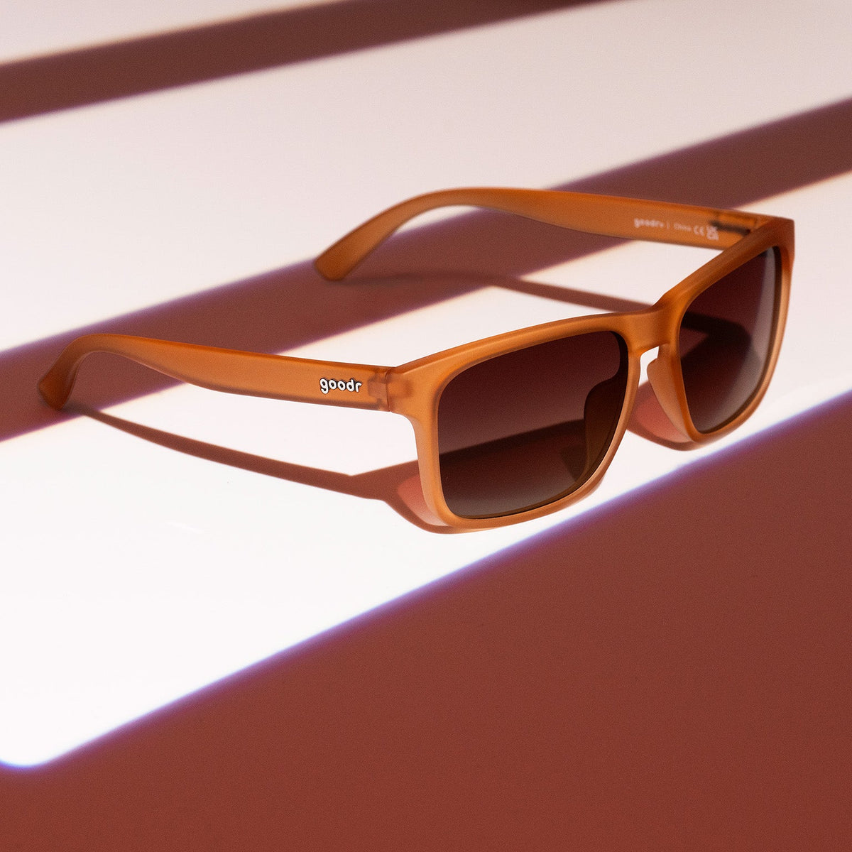 Three-quarter angle view of rich brown Grand Gs with brown-gray gradient lenses on a brown striped surface.