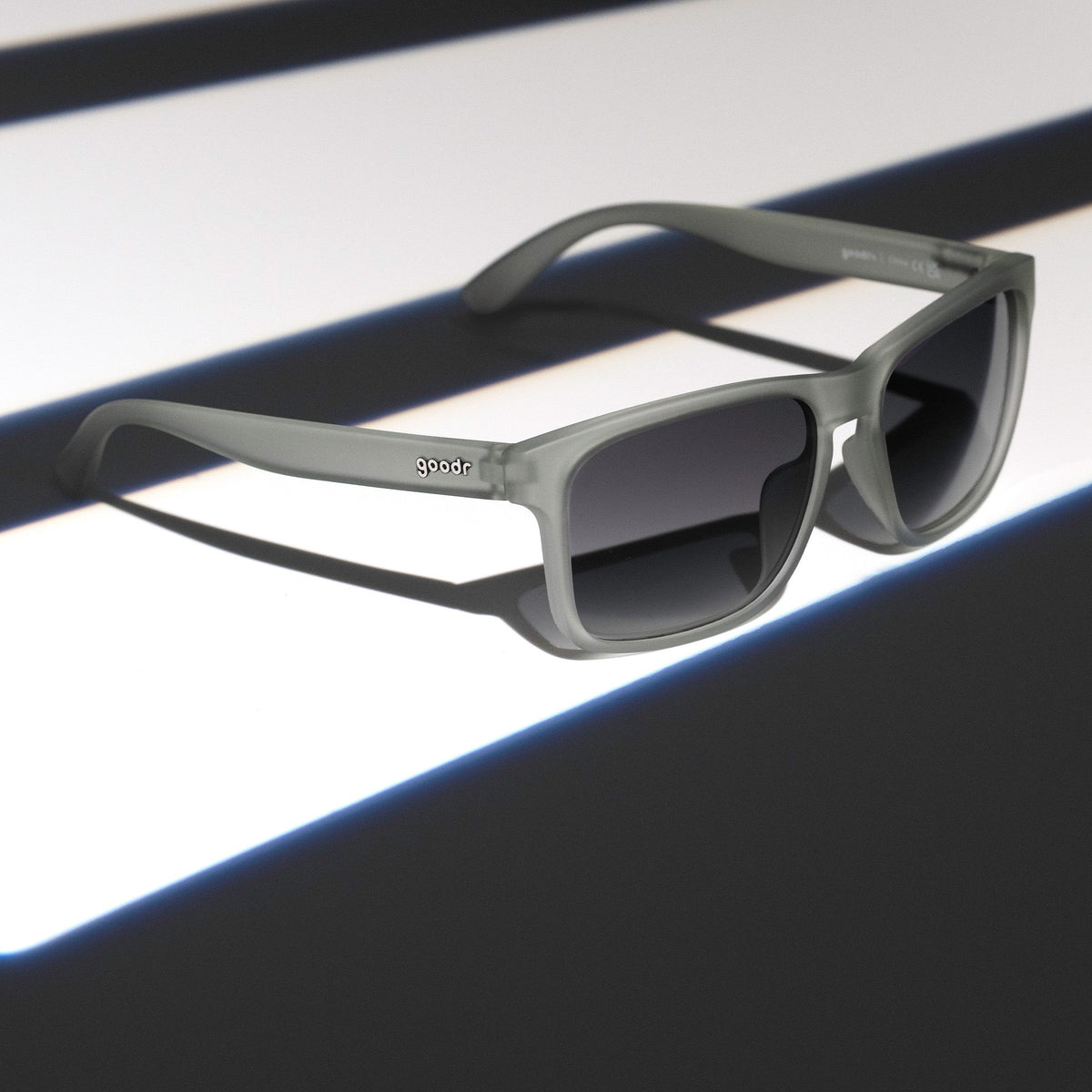 Three-quarter angle view of translucent gray Grand Gs with black gradient lenses on a dark gray striped surface.