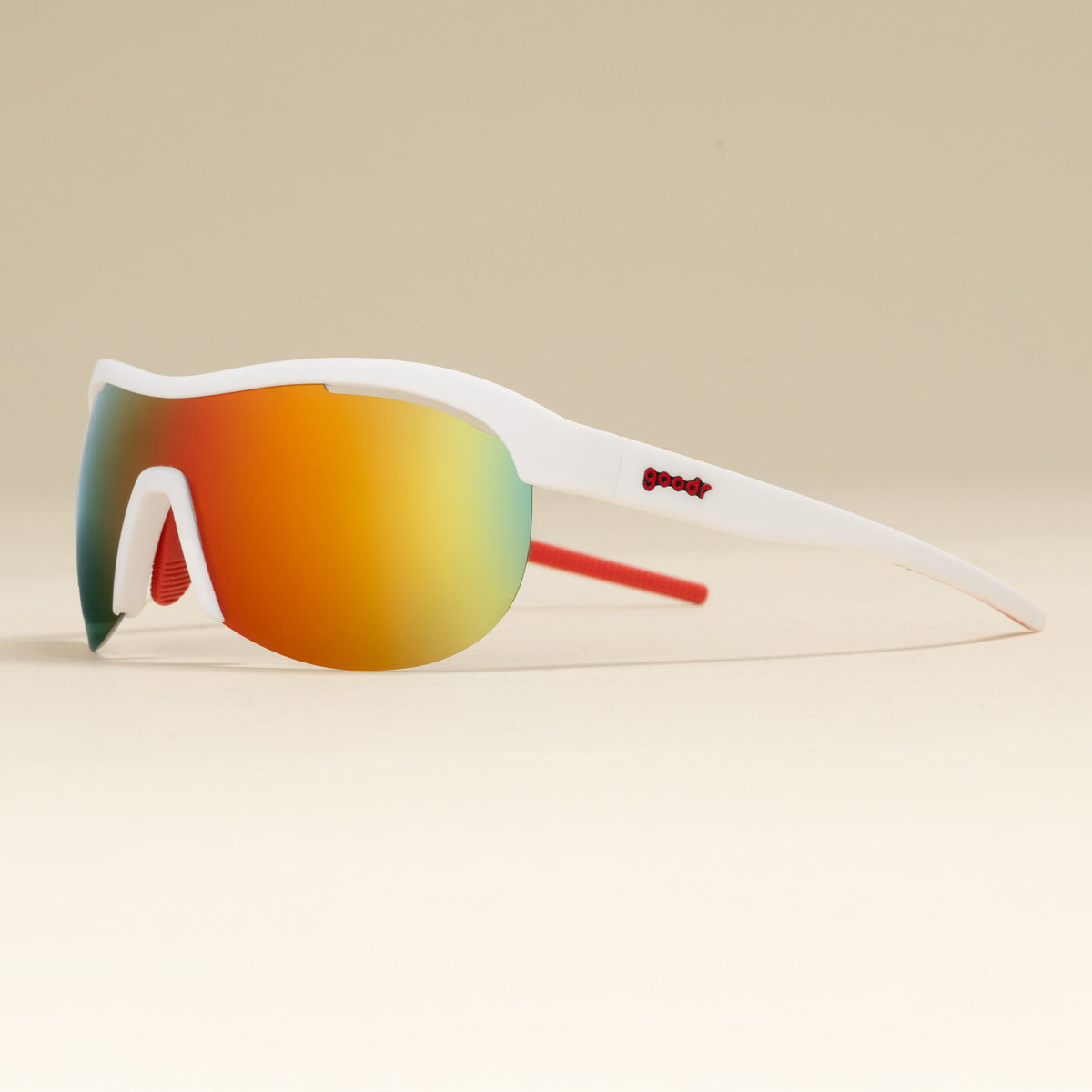 Left three-quarter angle view of white wrap shield sunglasses with red accents and fire-red reflective lenses on a tabletop.