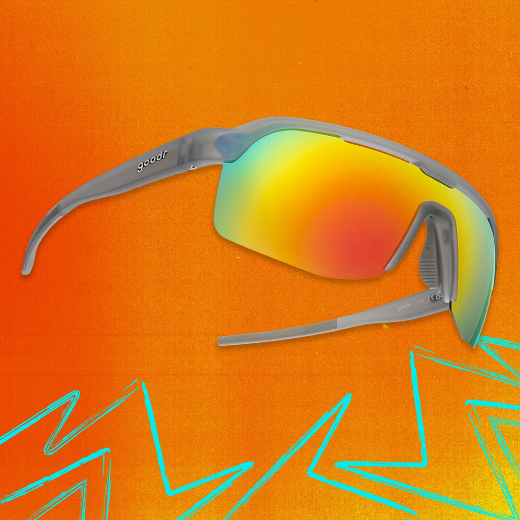 Three-quarter angle view of gray shield sunglasses with orange reflective wrap lenses tilted up on an orange background.