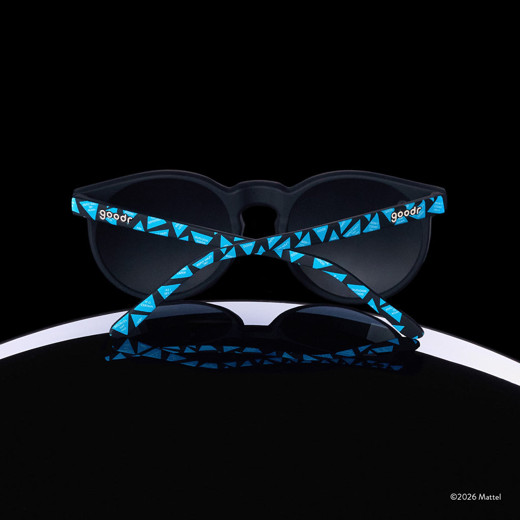 A pair of Magic 8 Ball-themed goodr sunglasses is perched atop the curve of an 8 ball, photographed from behind.