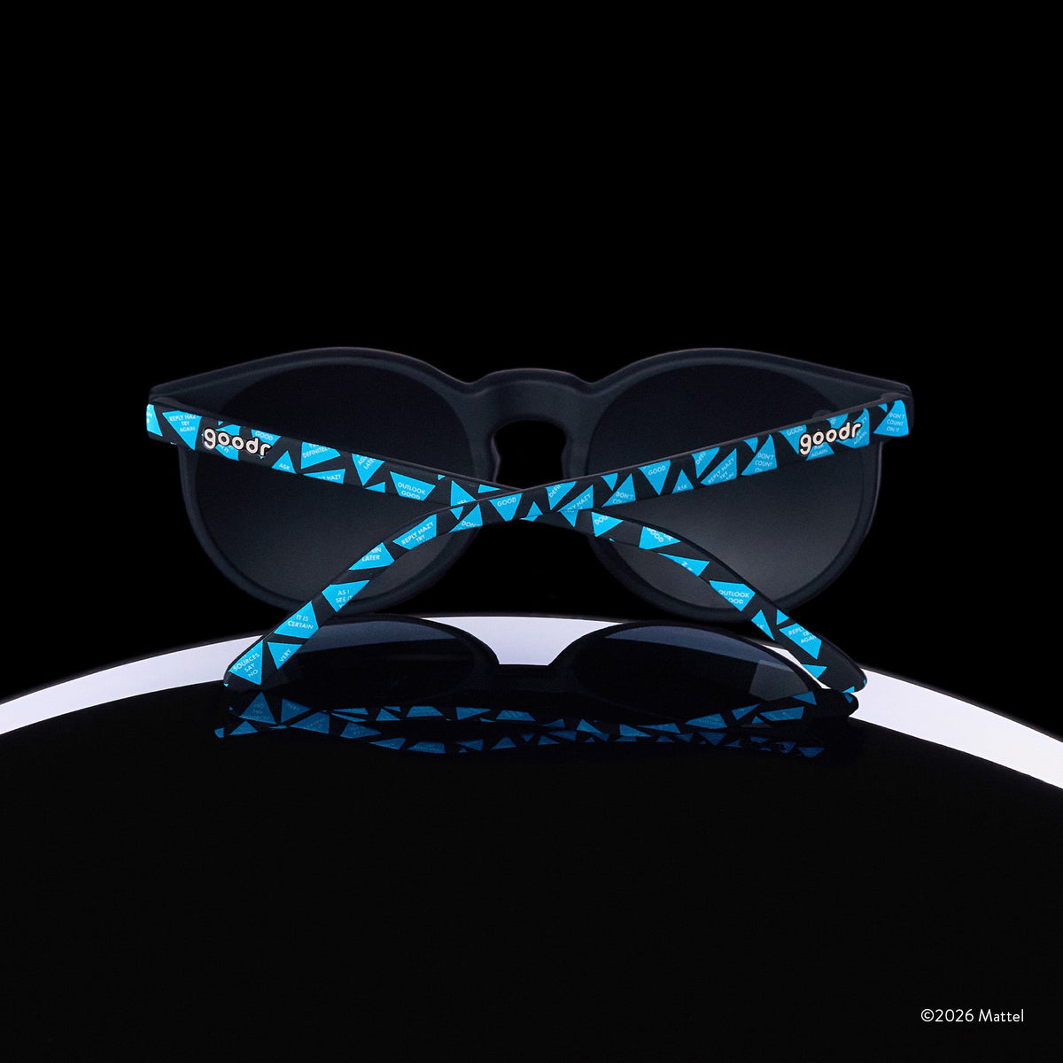 A pair of Magic 8 Ball-themed goodr sunglasses is perched atop the curve of an 8 ball, photographed from behind.