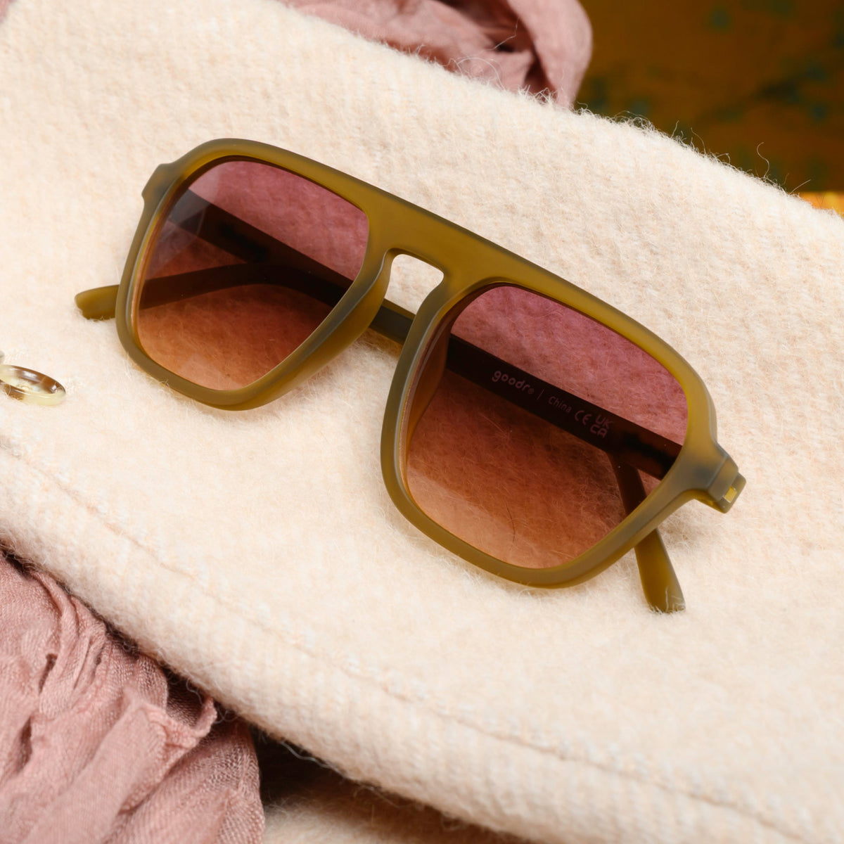 A pair of translucent ochre Retro G sunglasses sits folded atop a woolly, cream-colored jacket sleeve.