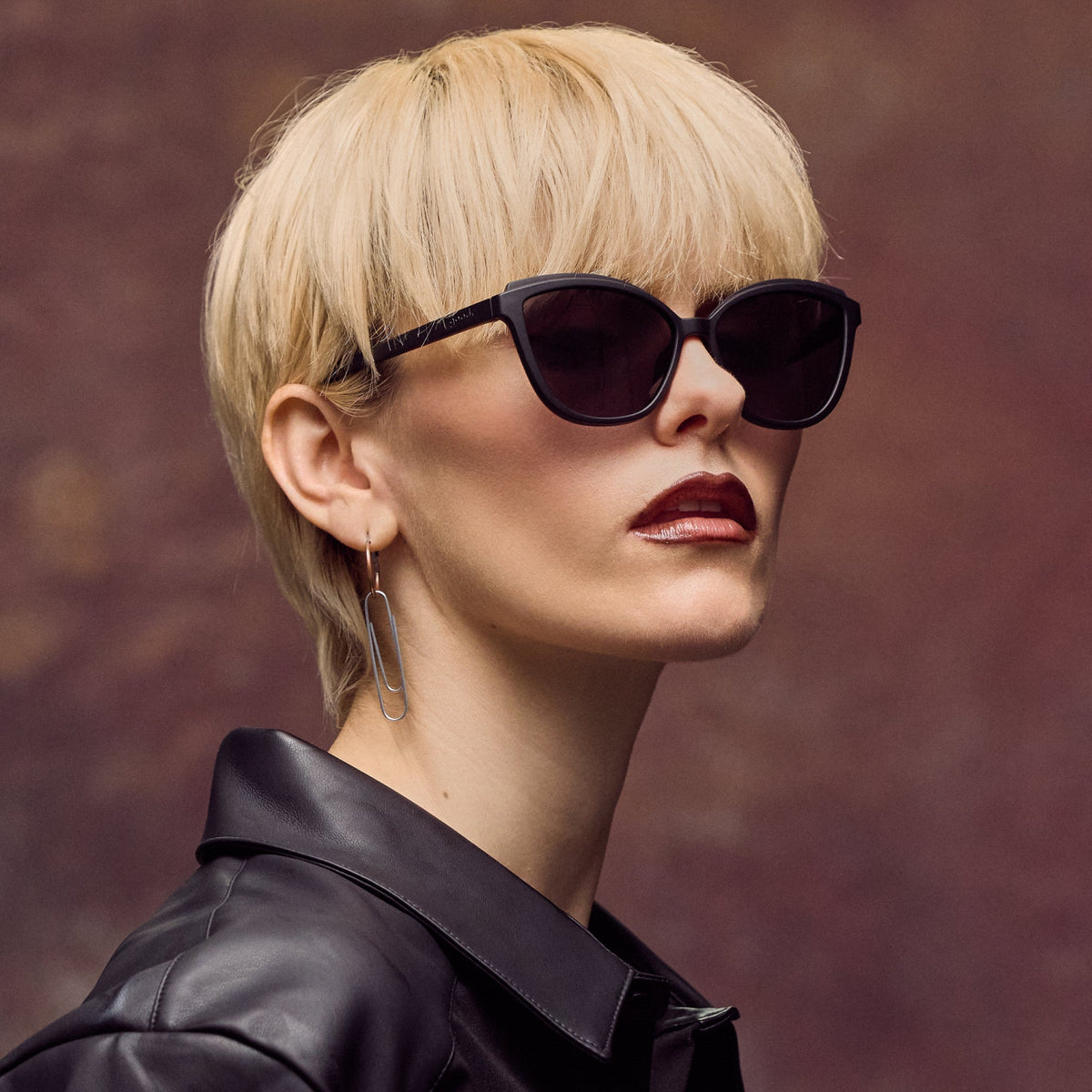 Woman wearing sunglasses and a black leather jacket against a brown background