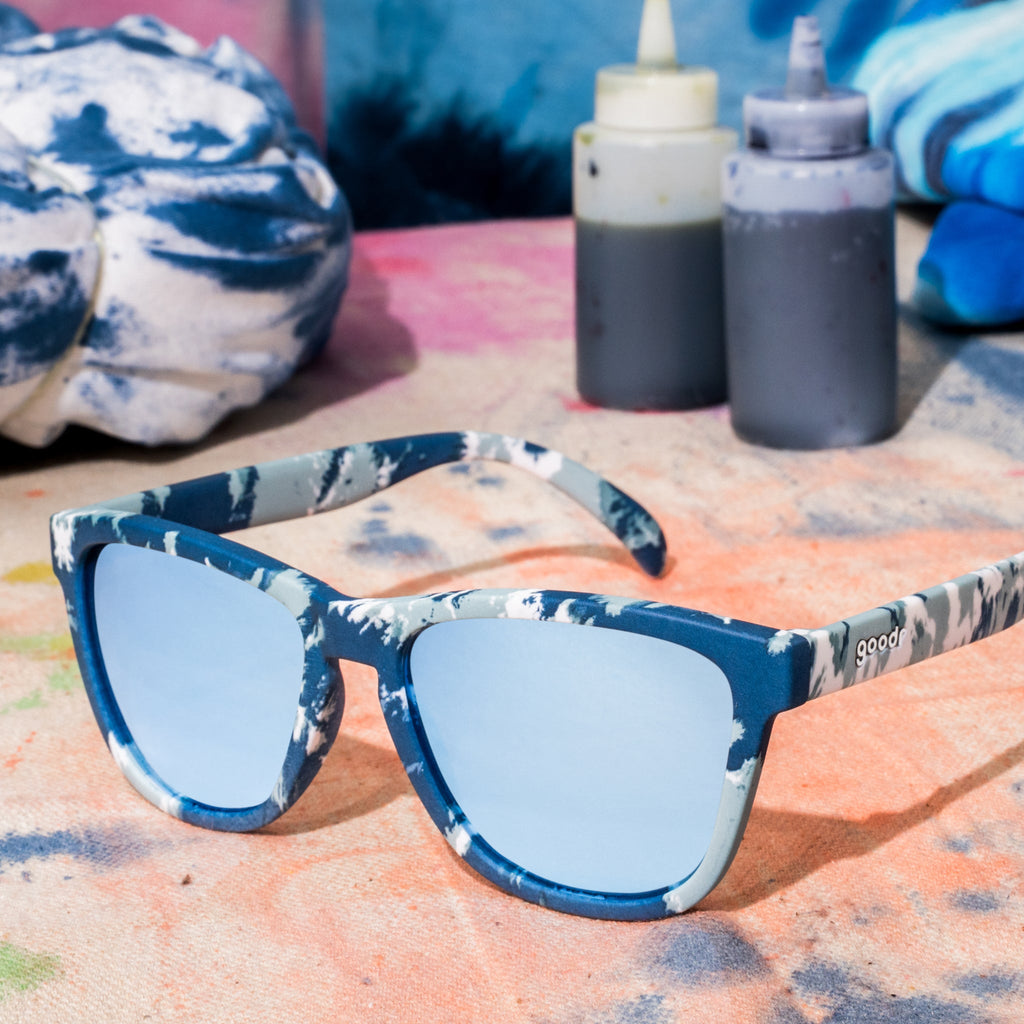 Blue tie-dye sunglasses sitting on a ball of white fabric tied with rubber bands, in the process of being tie-dyed blue.