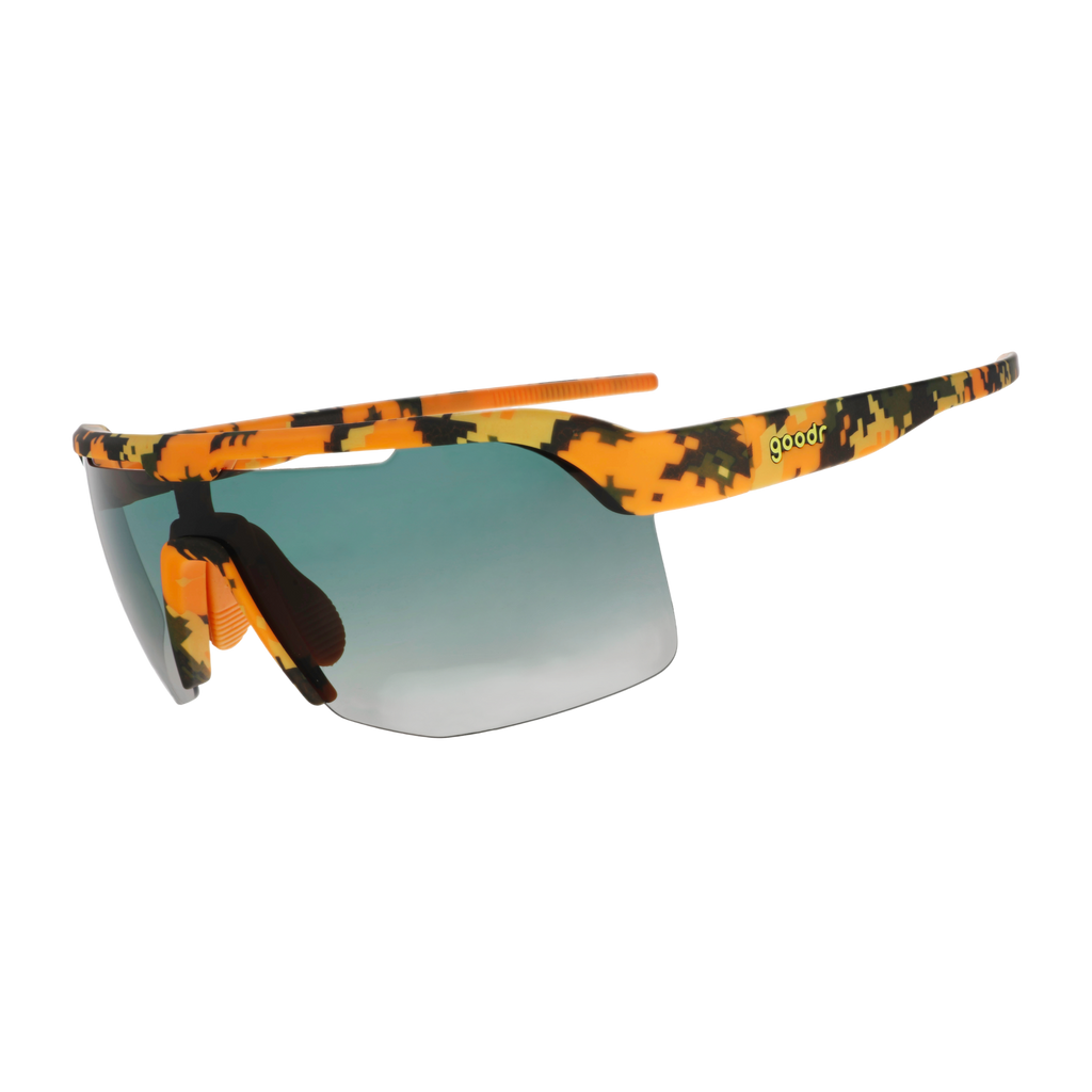 Sport sunglasses with a vibrant orange, yellow, and black camouflage pattern on the frame and arms, featuring a green-to-gray gradient lens and a small green 'goodr' text logo on the temple.