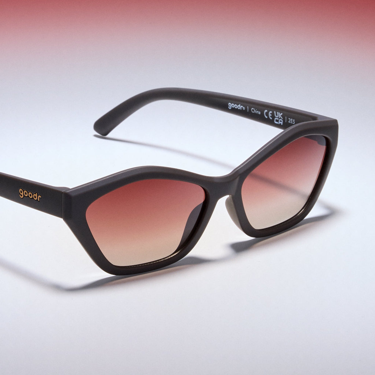 Sunglasses with black frame and red-tinted lenses on a gradient background